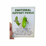 A collection of inspirational charms with humorous and supportive messages, including a blue bra charm, a potato with a sunburn, a taco, and a pickle. 