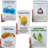 A collection of inspirational emotional support charms with humorous and supportive messages, including a blue bra charm, a potato with a sunburn, a taco, and a pickle. 