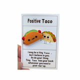 A collection of inspirational charms with humorous and supportive messages, including a blue bra charm, a potato with a sunburn, a taco, and a pickle. 