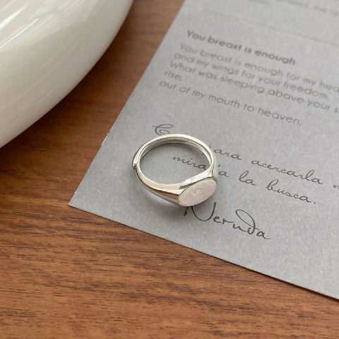 Silver ring with an opal stone on a wooden surface with text