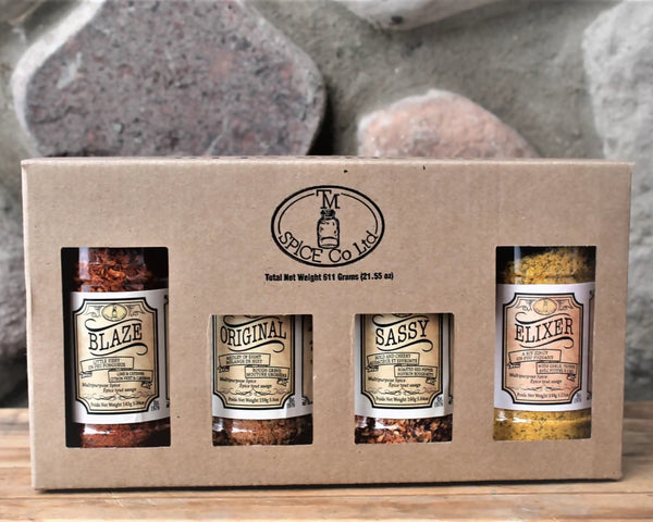 A signature gift box from TM Spice Blend featuring four bottles of spice in a cardboard packaging with a rustic design.