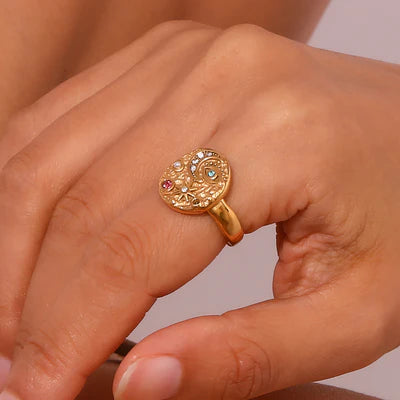 Gold ring with gemstones on a person's finger against a neutral background