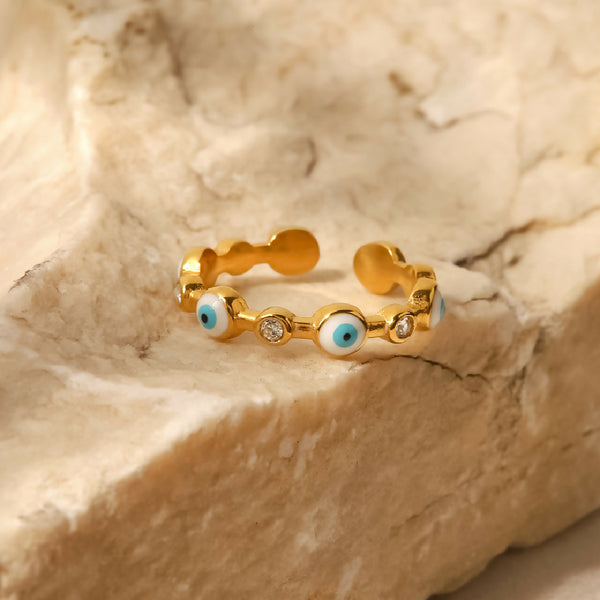 Gold ring with blue eye designs on a textured beige surface