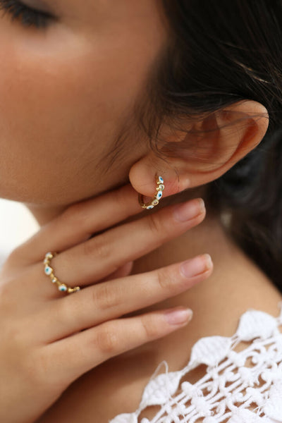 Close-up of a person wearing gold hoop earrings with small enamel evil eye charms.