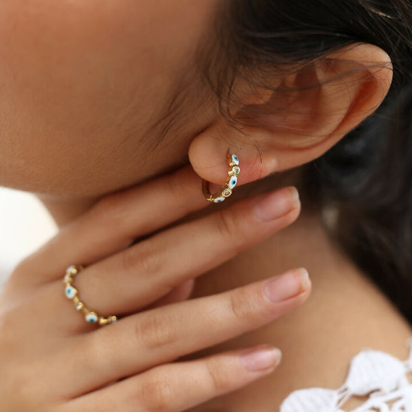 Close-up of a person wearing gold hoop earrings with small enamel evil eye charms.