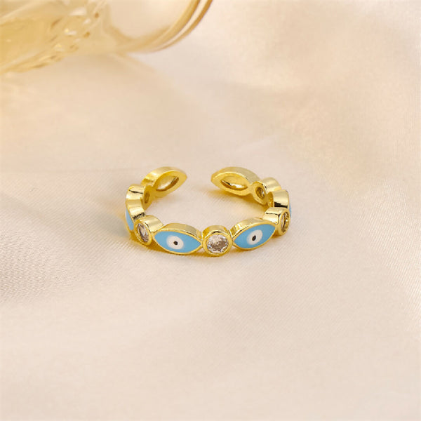 Gold ring with blue eye design on a beige background