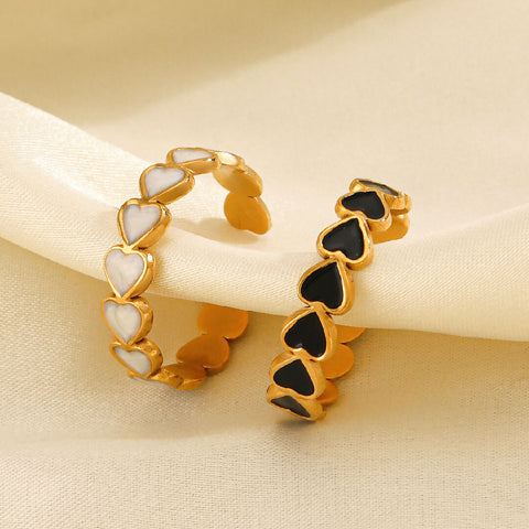 Two heart-shaped rings, one gold with white hearts and the other gold with black hearts, on a beige fabric background.