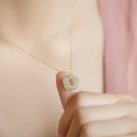 Necklace with a a gold chain and jade floral pendant held by a hand against a soft pink background
