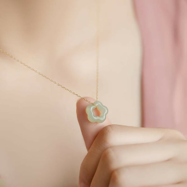 Necklace with a a gold chain and jade floral pendant held by a hand against a soft pink background