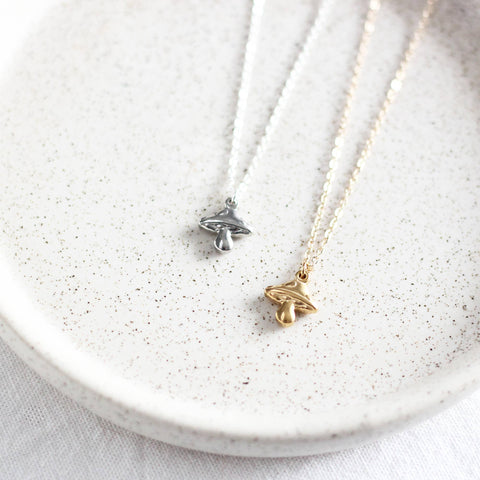 Two necklaces with mushroom pendants on a white speckled plate.