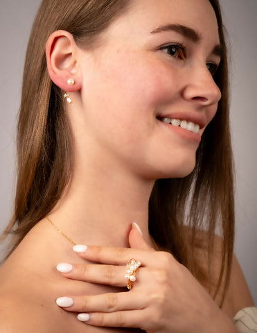 Woman wearing gold earrings and a pearl cluster ring, with a neutral background