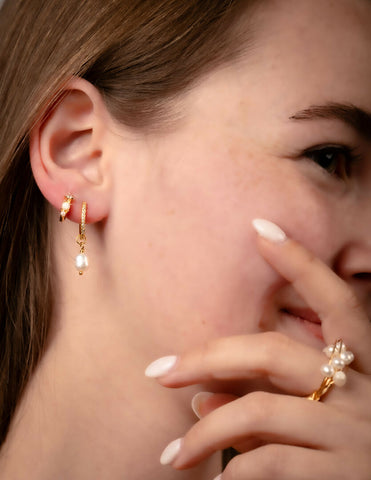 Close-up of a person wearing gold earrings and a ring with pearl accents.