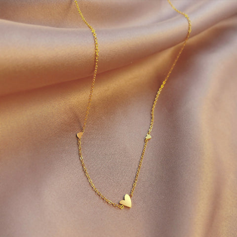 Gold necklace with heart pendants on a soft pink fabric background