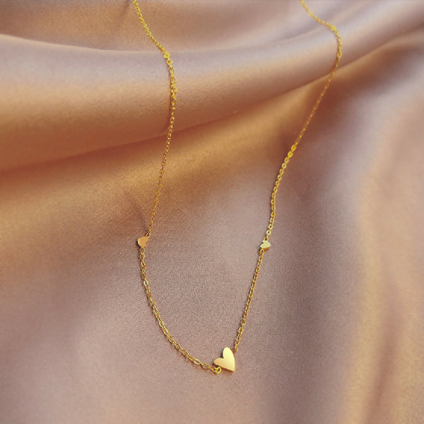 Gold necklace with heart pendants on a soft pink fabric background